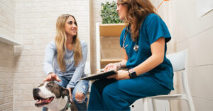 female dog owner sitting with dog while talking with vet about yearly dog vaccinations